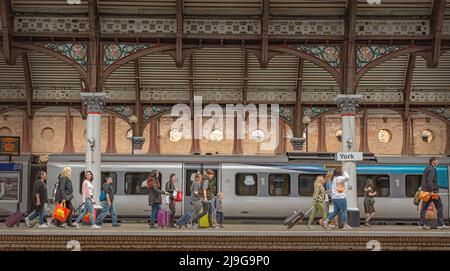 Eine Reihe von Fahrgästen auf einem Bahnhofsplatz, die einen Zug verlassen. Ein historisches Vordach befindet sich über dem Dach. Stockfoto