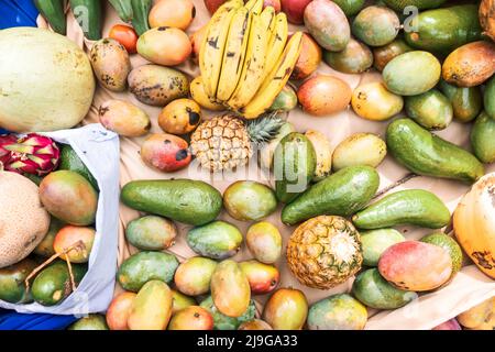 Draufsicht auf tropische Früchte auf Stoffhintergrund. Mangos, Avocados, Ananas, Bananen und andere tropische Früchte. Konzept der Lebensmittelproduktion in Stockfoto
