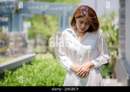 Eine asiatische Frau berührt ihren Magen aufgrund von Magenschmerzen und unerwünschten Symptomen. Stockfoto