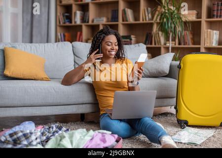 Aufgeregt afroamerikanische Dame mit Laptop und telefonieren während der Suche Sommerurlaub, Vorbereitung auf den Urlaub Stockfoto