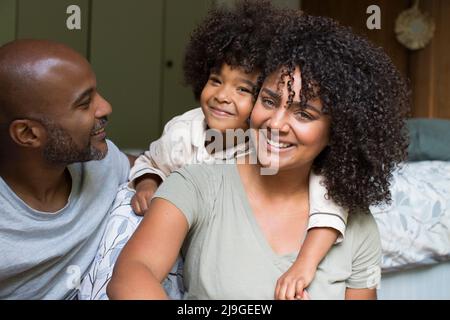 Lächelnde Familie sitzt zusammen auf dem Bett Stockfoto