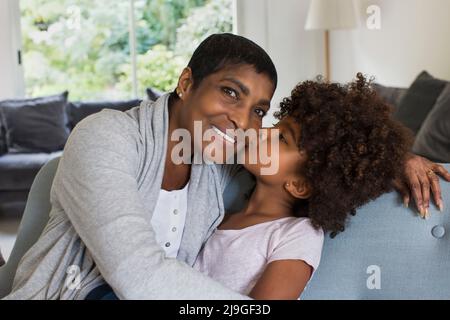 Enkelin küsst Großmutter im Wohnzimmer Stockfoto