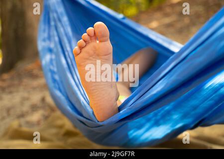 Kinderfuß in einer Hängematte, rollend im Wald im Sommer in der Sonne, Rest in einer Hängematte, ein Fuß in einer Hängematte, Rest im Wald Stockfoto