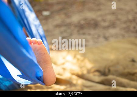 Kinderfuß in einer Hängematte, rollend im Wald im Sommer in der Sonne, Rest in einer Hängematte, ein Fuß in einer Hängematte, Rest im Wald Stockfoto