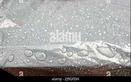 Wasser fließt in Tropfen verschiedener Größen auf einem Oilcloth. Regentropfen auf der Oberfläche. Selektiver Fokus Stockfoto