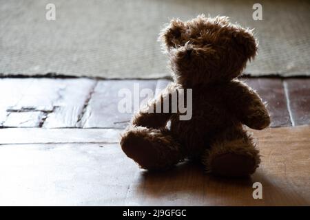 Brauner Teddybär sitzt auf einem alten Holzboden in einem dunklen Raum, Kinderspielzeug auf dem Boden, Angst Stockfoto