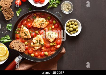 Kabeljaueintopf mit Kichererbsen, Kirschtomaten und Oliven in einer Pfanne auf dunklem Steingrund. Draufsicht, flach liegend Stockfoto