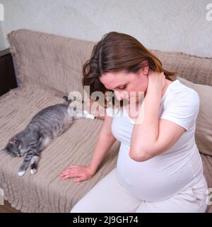 Eine Schwangere hält sich an einen schmerzenden Hals im häuslichen Interieur, Lebensstil Stockfoto