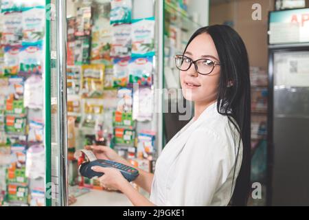 Apotheke und der Verkäufer. Eine Frau mit Brille kauft mit einer Bankkarte über ein mobiles Endgerät. Stockfoto