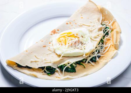 Pfannkuchen gefüllt mit Spinatblättern, serviert mit Spiegelei und geriebenem Käse Stockfoto