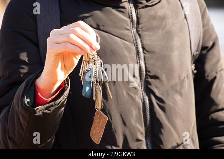 Das Mädchen hält in den Händen die Schlüssel zur Wohnung auf der Straße in der Sonne, die Schlüssel zum Haus, Kauf und Vermietung von Immobilien Stockfoto