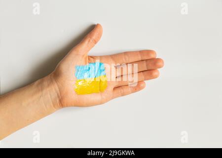 Die Flagge der Ukraine ist gelb-blau auf der Hand eines Mädchens gemalt. Kriegsrecht in der Ukraine 2022. Stoppt Krieg und Frieden Stockfoto