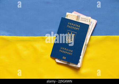 Biometrischer Auslandspass mit Geld liegt auf der Nationalflagge der Ukraine gelb-blau Stockfoto