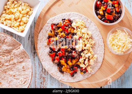 Gesunde proteinreiche Burritos mit Eiern, Paprika, Süßkartoffeln, schwarzen Bohnen auf Vollkorntortillas mit geriebenem Käse, Draufsicht. Gesundes Frühstück Stockfoto