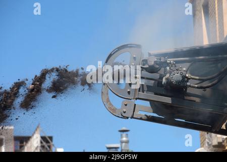 Das Straßenfräsfahrzeug lädt gefrästen Asphalt in einen Muldenkipper in einem engen Innenhof mit alten Häusern. Stockfoto
