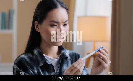 Verwirrt zweifelhafte asiatische Frau warten Ergebnis der Schwangerschaft Test Mädchen Sorgen mit ungeplanten Kindern. Traurige unglückliche, schwanger koreanische Dame, die zu Hause sitzt Stockfoto