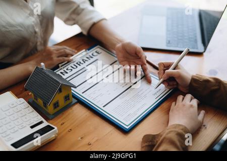 Immobilien zeigen auf die Unterzeichnung des Versicherungsvertrags und erklären den Kunden im Büro Stockfoto