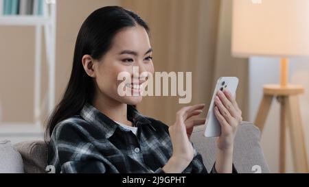 Lächelnd glücklich asiatische Frau Eingabe Swipe Touchscreen des Telefons Koreanisches Mädchen fröhlich Wahl Einkaufen in Online-E-Commerce-App weiblich genießen mobil Stockfoto