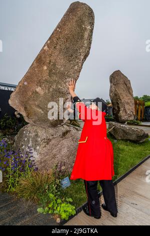 London, Großbritannien. 23.. Mai 2022. Eine weibliche Rentnerin aus Chelsea scheint eines von Adrian Grays monumentalen Steinbalancierungsstücken ‘stabil' zu sein - ein 6 Tonnen schwerer kornischer Granitfelsen, der sich prekär kippt und 4 Meter vom Boden entfernt erhebt - die Chelsea Flower Show 2022. Kredit: Guy Bell/Alamy Live Nachrichten Stockfoto