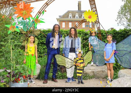 Chelsea, London, Großbritannien. 23.. Mai 2022. Danny Clarke und Tayshan Hayden-Smith mit den Kindern. Im „Hands Off Mangrove by Grow2Know“-Garten posieren Kinder in farbenfrohen Notting Hill Carnival-Kostümen, die von Denis George unter der Leitung von Carl Gabriel entworfen und entworfen wurden und von den beiden überlebenden Mangrove Nine-Mitgliedern begleitet werden. Der Chelsea Flower Show Press Day sieht eine Vorschau der Show vor, die in das Royal Hospital Chelsea zurückkehrt und dieses Jahr vom 24. Bis 28. Mai stattfindet. Kredit: Imageplotter/Alamy Live Nachrichten Stockfoto