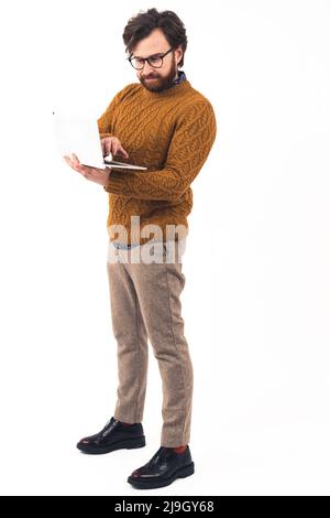 Ganzkörperaufnahme. Gutaussehender bärtiger Unternehmer, der seinen Laptop hält und auf die Tastatur klickt. Vertikale Studioaufnahme mit weißem Hintergrund. Hochwertige Fotos Stockfoto
