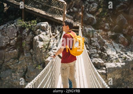 Vater und Sohn blicken beim Wandern weit von der Seilbrücke in die Berge. Lässig gekleidete Touristen Kinderschultjunge und sein Vater mit gelb Stockfoto