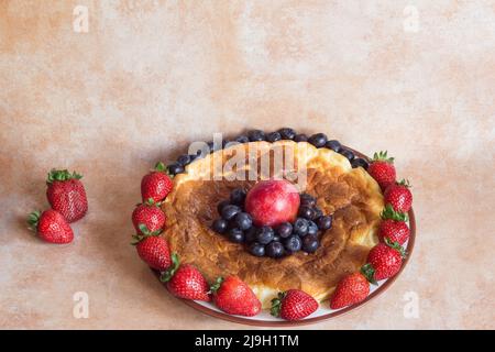 Ein köstlicher und farbenfroher Käsekuchen, der mit Erdbeeren, Blaubeeren und Pflaumen auf einem Marmortisch und ein paar Erdbeeren daneben dekoriert ist. Essen und er Stockfoto