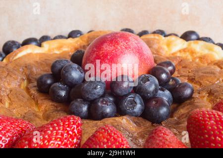 Nahaufnahme einer Gruppe von Heidelbeeren, die eine rote Pflaume auf einem Erdbeerkäsekuchen umgaben. Gesunde Desserts und Früchte. Stockfoto