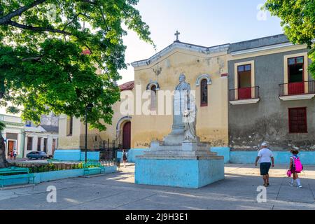 Die Kubaner gehen in einem kleinen öffentlichen Park an einer alten Skulptur von Manuel de Jesus Doval vorbei. Die Parroquia de Jesús, María y José, die eine Kolonialkirche ist Stockfoto