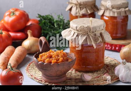 Hausgemachter Gemüsekaviar aus Karotten, Paprika, Knoblauch und Tomaten in Schüssel und Gläsern auf hellgrauem Hintergrund Stockfoto