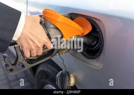 Die Hand einer Frau hält eine Tankpistole in den Hals des Panzers des Autos. Das Mädchen betankt das Auto Stockfoto