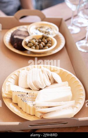 Käse, Oliven und Brot werden auf umweltfreundlichen pflanzlichen Tellern und Papptablett für eine freundliche Party in einem Weingut, einer Bar oder einem Restaurant serviert. Stockfoto