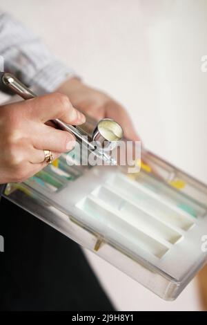 Nahaufnahme der Hände einer Konditorin, die beim Herstellen von Pralinen mit einer Airbrush in der Küche Lebensmittelfarbe sprüht. Stockfoto