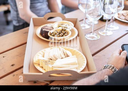 Käse, Oliven und Brot werden auf umweltfreundlichen pflanzlichen Tellern und Papptablett für eine freundliche Party in einem Weingut, einer Bar oder einem Restaurant serviert. Stockfoto