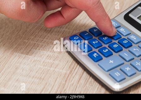 Nahaufnahme der Hand einer Person, die die Acht-Taste auf der Tastatur eines grauen Rechners mit blauen Tasten auf einem Holztisch drückt. Stockfoto