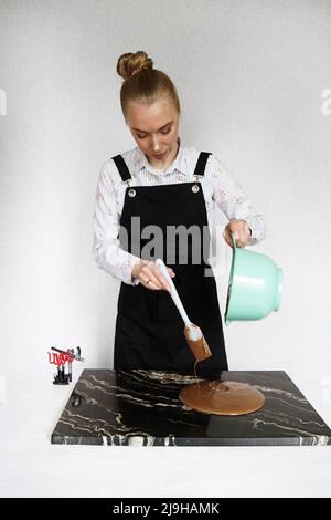 Nahaufnahme - Frau rührt Schokolade und gießt auf einem Steinbrett für die Herstellung von hausgemachten Pralinen. Süßwarenherstellung, Konditorei, Dessertkonzept Stockfoto