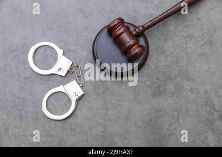 Thema „Recht“. Gerichtsverfahren in Sitzung. Richter Gavel Handschellen auf grauen Tisch in Anwaltsbüro oder Gerichtsverhandlung. Mallet von Richter auf Beton Stein grauen Hintergrund. Gerechtigkeit Menschenrechte Konzept Stockfoto