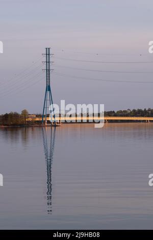 Helsinki / Finnland - 22. MAI 2022: Hoher Strommast, der während des Sonnenuntergangs auf das ruhige Wasser reflektiert. Stockfoto