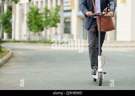 Beschnittenes Bild eines Unternehmers in Anzug, der auf einem E-Scooter zu einem Geschäftstreffen fährt Stockfoto