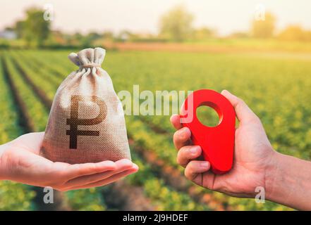 Hände mit Positionsnadel und russischem Rubel-Geldbeutel. Schätzkosten der Plots. Landwirtschaft in der Landwirtschaft. Transport- und Bauindustrie. Kauf eines Stockfoto