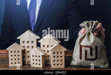 Ein Geschäftsmann legt einen israelischen Schekelgeldbeutel in die Nähe der Häuser. Bauindustrie, Vermietung und Hoteltourismus. Städtisches Budget der Stadt. Stockfoto