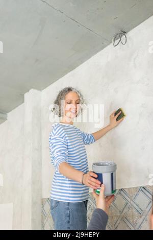 Lächelnde Frau mit Freund, der die Wand in einem neuen Zuhause schrubbt Stockfoto