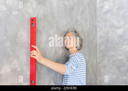 Lächelnde Frau mit einem Füllstandmessgerät an der grauen Wand Stockfoto