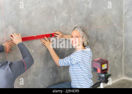 Lächelnde Frau mit Freund, die zu Hause die Ebene an der grauen Wand benutzt Stockfoto