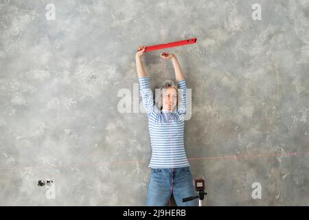 Glückliche Frau, die das Messwerkzeug vor der grauen Wand hält Stockfoto