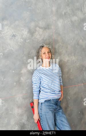 Lächelnde Frau, die sich auf einer Ebene an einer grauen Wand lehnte Stockfoto