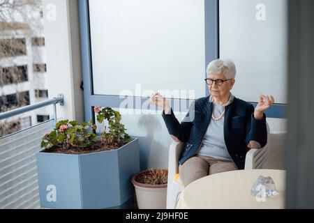 Ältere Frau meditiert auf dem Balkon Stockfoto