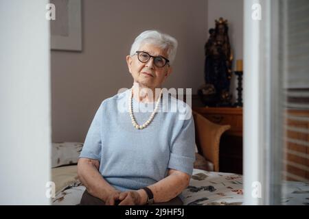 Einsame ältere Frau, die zu Hause im Schlafzimmer auf dem Bett sitzt Stockfoto