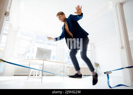 Glücklicher Geschäftsmann, der im Büro auf Gratwanderung ausbalanciert Stockfoto