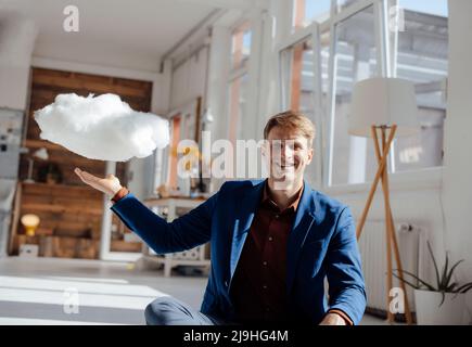 Glücklicher Geschäftsmann mit schwebendem Cloud-Netzwerk im Büro Stockfoto